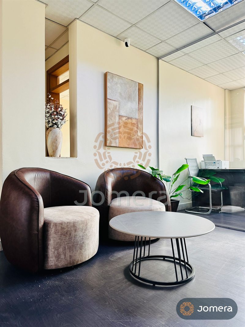 Office waiting area with leather-backed swivel tub chairs, a round sintered-stone coffee table, textured abstract art and a niche vase of blossom