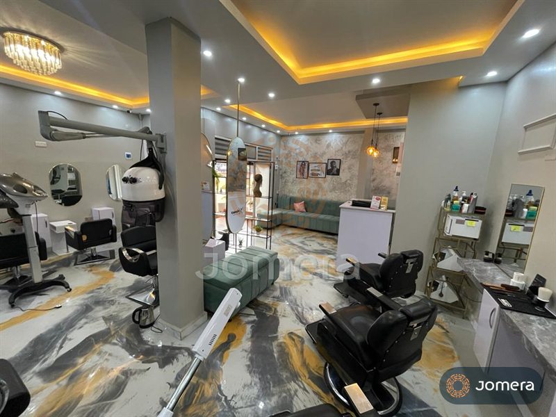 Wide view of a salon with a warm cove-lit stepped ceiling, crystal chandelier, styling stations, a sage lounge and a marbled epoxy floor